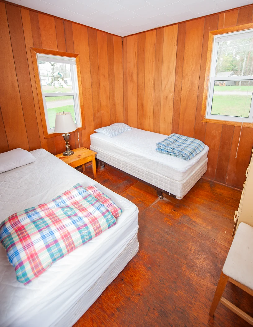 Pigeon Lake Resort Cottage five, bedroom with two single beds, wood-paneled walls, windows, and bedside table with lamp.